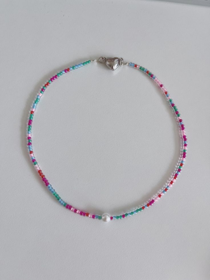 a beaded bracelet with pink, blue and green beads on a white surface next to a silver charm