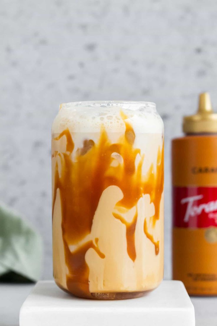 an iced drink sitting on top of a white table next to a can of soda