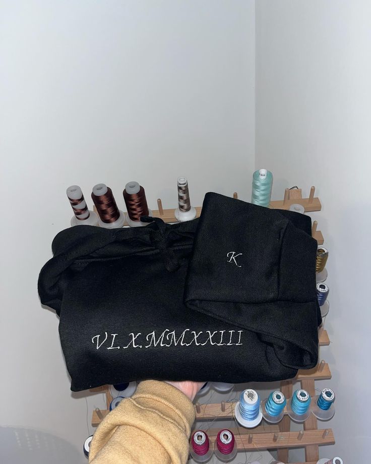 a person holding onto a black bag with thread spools on it next to other items