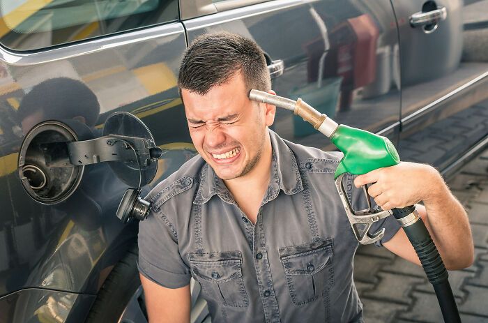 a man is pumping gas into his car at the pump, and he is smiling