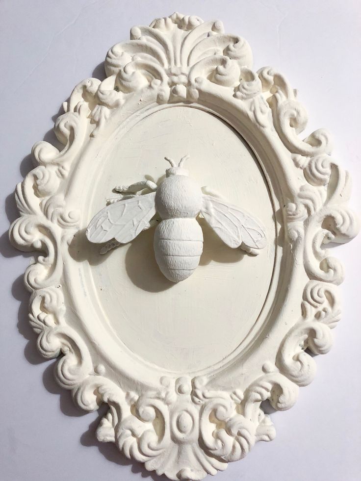 a white plate with a bee on it and ornate border around the edge, in front of a white wall