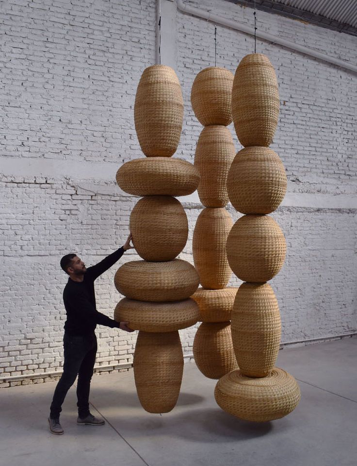 a man standing next to a tall sculpture made out of stacks of woven material on top of each other