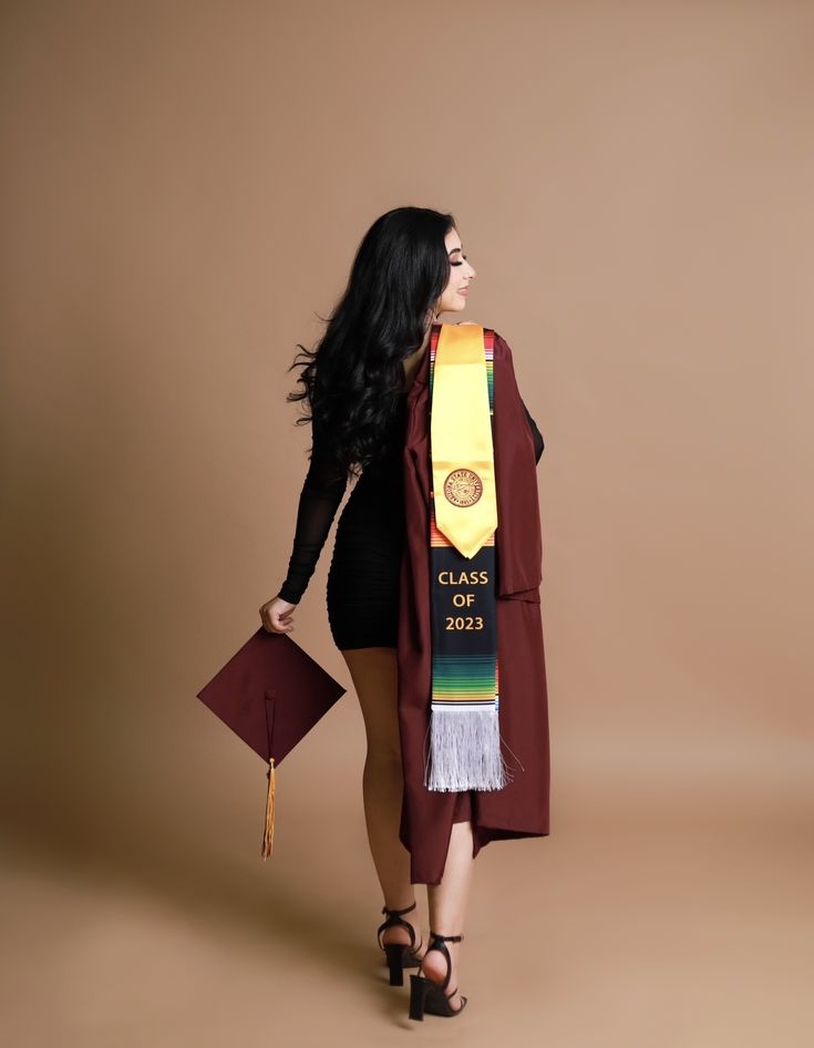 a woman wearing a graduation stole and holding a book in one hand while standing against a brown background