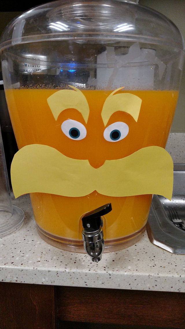 an orange juice machine with a paper mustache on it's face and eyes, sitting on a counter