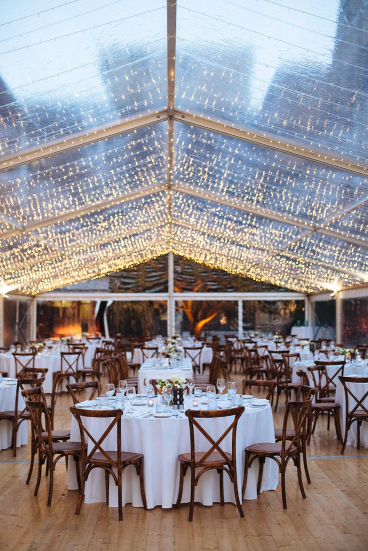 the inside of a large tent with tables and chairs set up for an elegant dinner