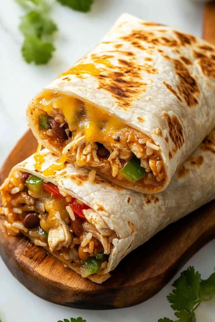 two burritos sitting on top of a wooden cutting board