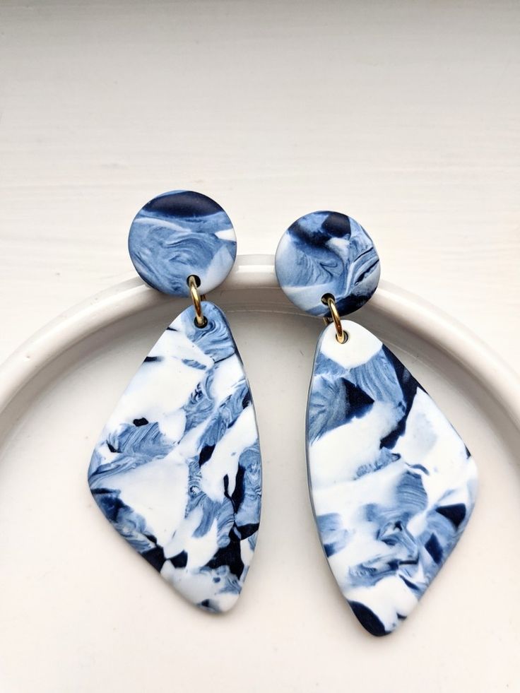 two blue and white earrings sitting on top of a white plate next to each other