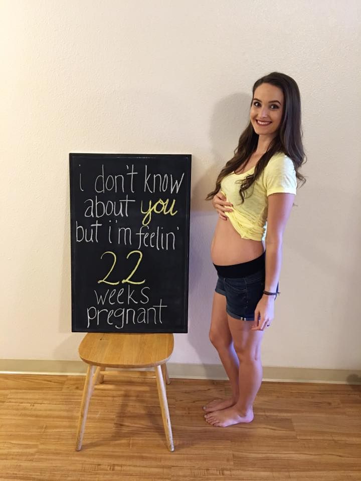 a pregnant woman standing in front of a chalkboard that says i don't know about you, but i'm telling 22 weeks pregnant