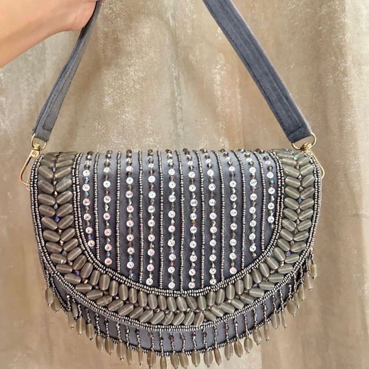 Introducing the Grey Shefali Flap Bag, a stunning fusion of elegance and Indian craftsmanship. Hand-beaded with luxurious velvet in enchanting hues of Grey, this bag embodies opulence and tradition. Its intricate design, coupled with delicate Grey bead work, this makes it a standout accessory for brides and lovers of Indian fashion alike. Whether for a wedding ceremony or a cultural celebration, the Shefali Grey Flap Bag adds a touch of regal charm to any outfit. Elevate your ensemble with the e Elegant Festival Bags, Elegant Festival Bags For Festive Occasions, Elegant Festive Bags For Festival, Festive Embellished Clutch Shoulder Bag, Festive Embellished Shoulder Bag For Evening, Festive Embellished Evening Shoulder Bag, Elegant Hand Embellished Festival Bag, Elegant Embellished Festival Bag, Festival Beaded Clutch Bag