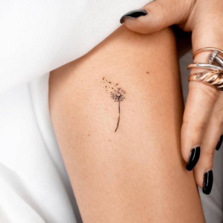 a woman's thigh with a small dandelion tattoo on her left side