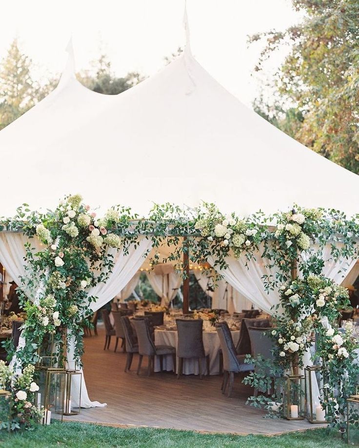 a white tent with tables and chairs covered in greenery