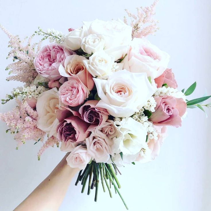 a bridal bouquet with pink and white flowers is held by a woman's hand