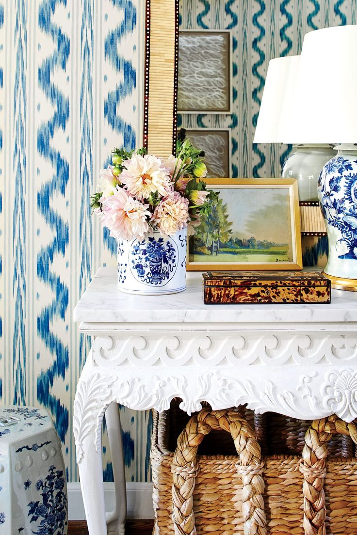 a white table topped with blue and white vases next to a wallpapered wall