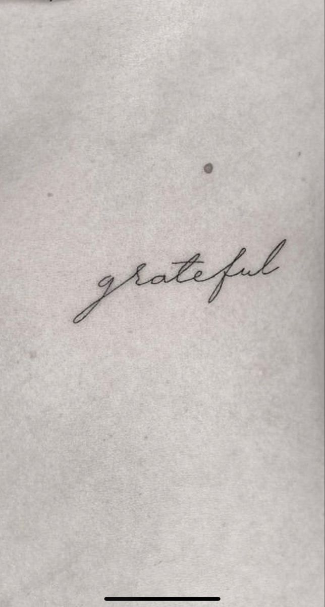 the word grateful written in cursive handwriting on a white paper sheet with a black dot