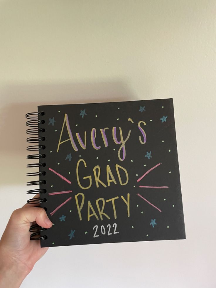 someone holding up a black notebook with the words avery's grad party on it