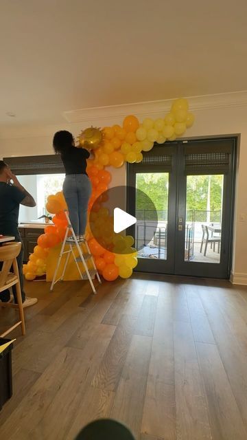 a woman is standing on a ladder in front of an arch made out of balloons