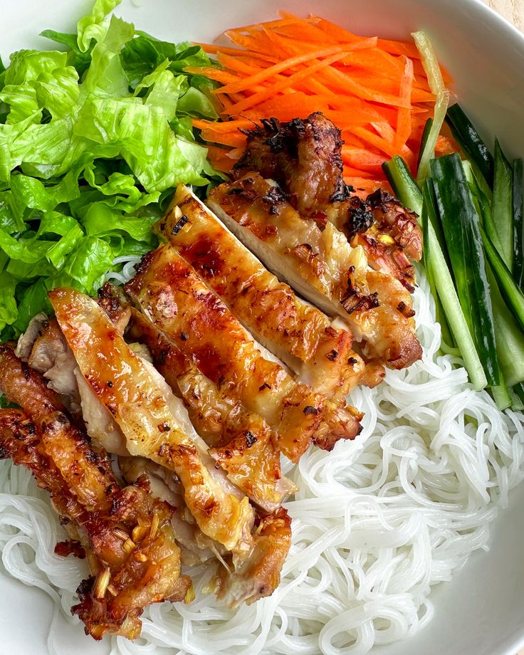 a white bowl filled with meat and veggies on top of rice next to carrots