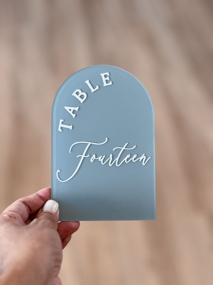 a person holding up a small blue table sign with the word table written on it