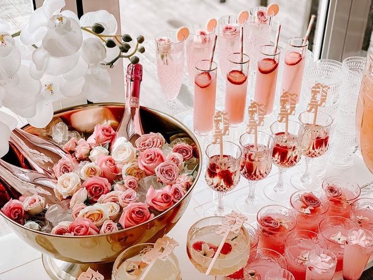 a table topped with lots of glasses filled with pink liquid and flowers next to champagne flutes