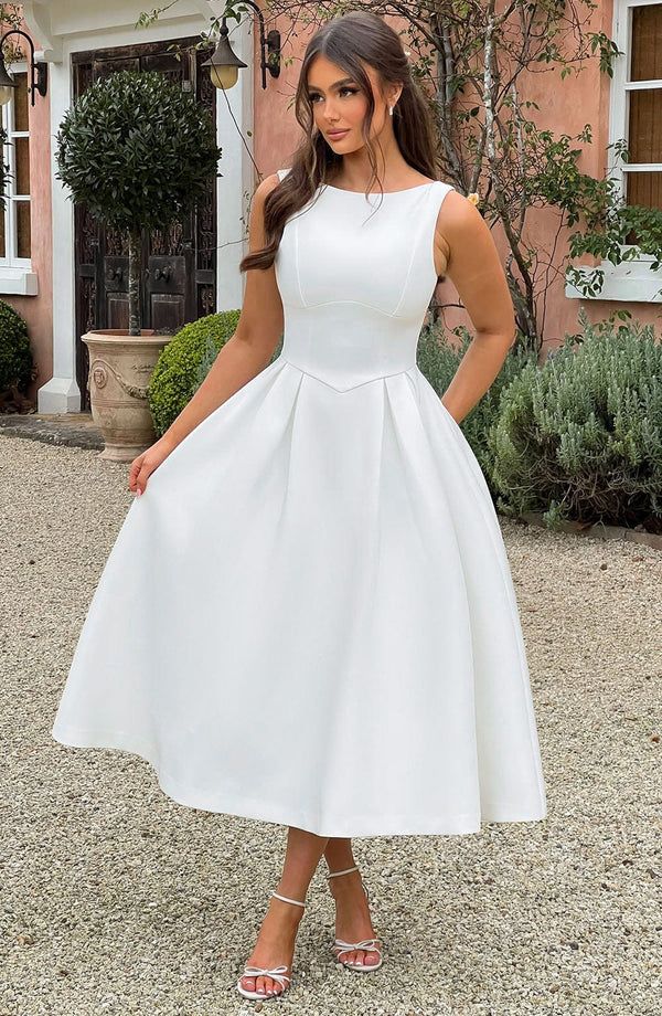 a woman standing in front of a building wearing a white dress and heels with her hands on her hips