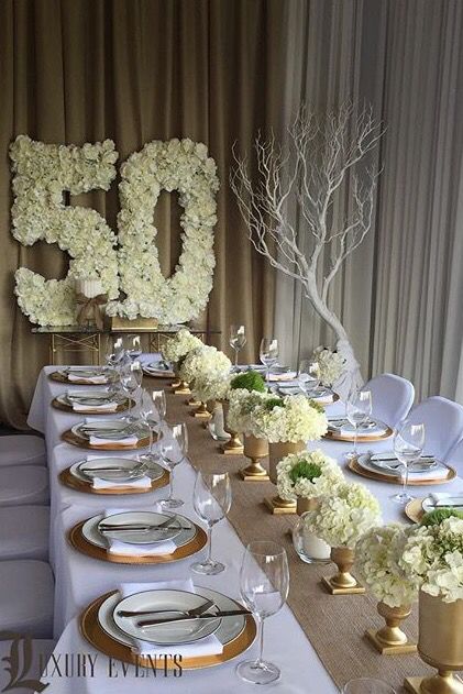 the table is set with white flowers and gold place settings for guests to sit at