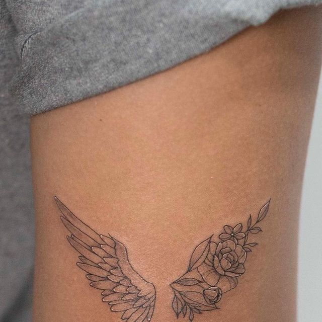 a woman's thigh with wings and flowers on the side, tattooing it