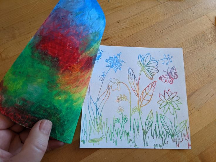 a child's hand holding a piece of paper next to an art project with flowers and butterflies on it