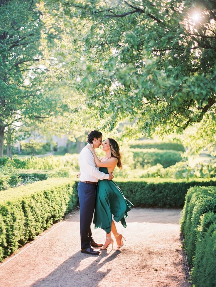 a man and woman embracing in the middle of a path surrounded by hedges at sunset