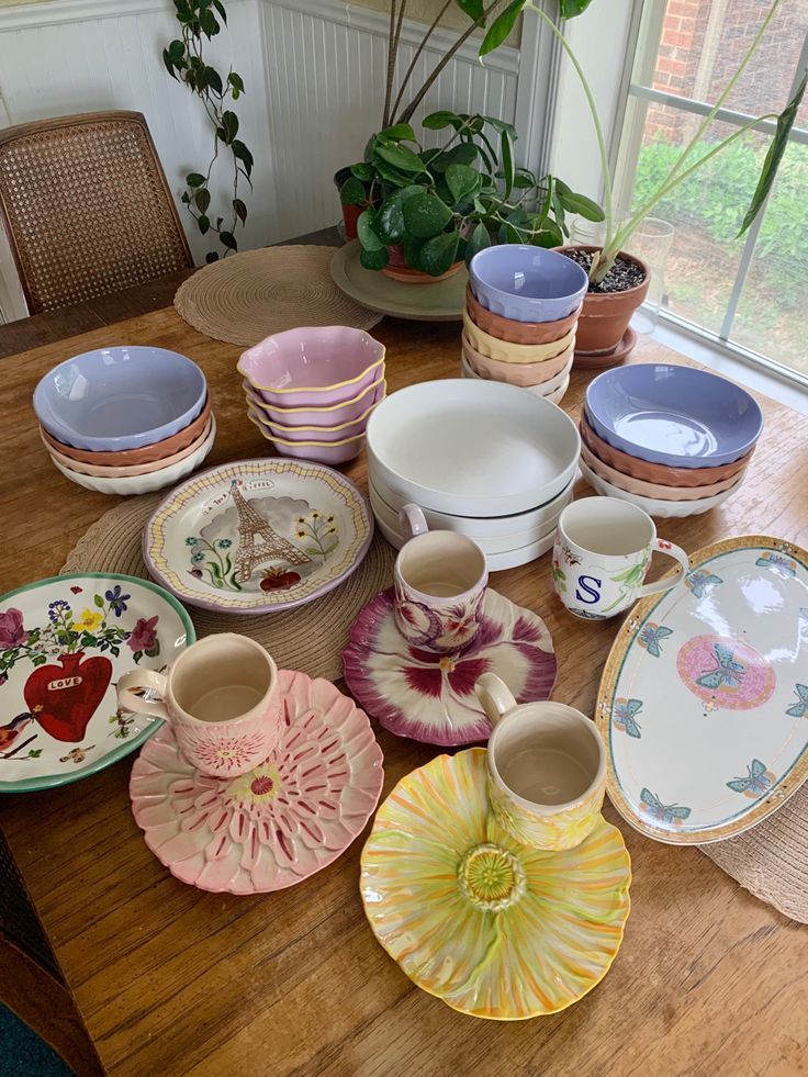 a wooden table topped with lots of plates and bowls next to a potted plant