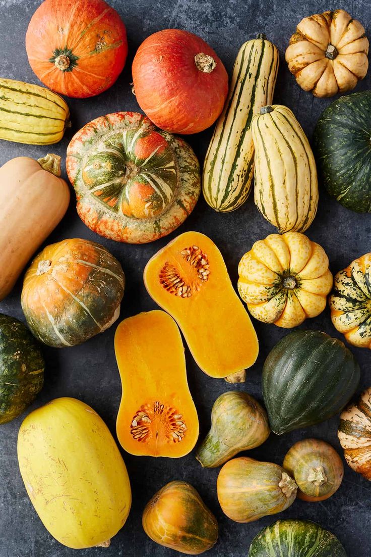 pumpkins, squash and gourds are arranged on a gray surface with black background