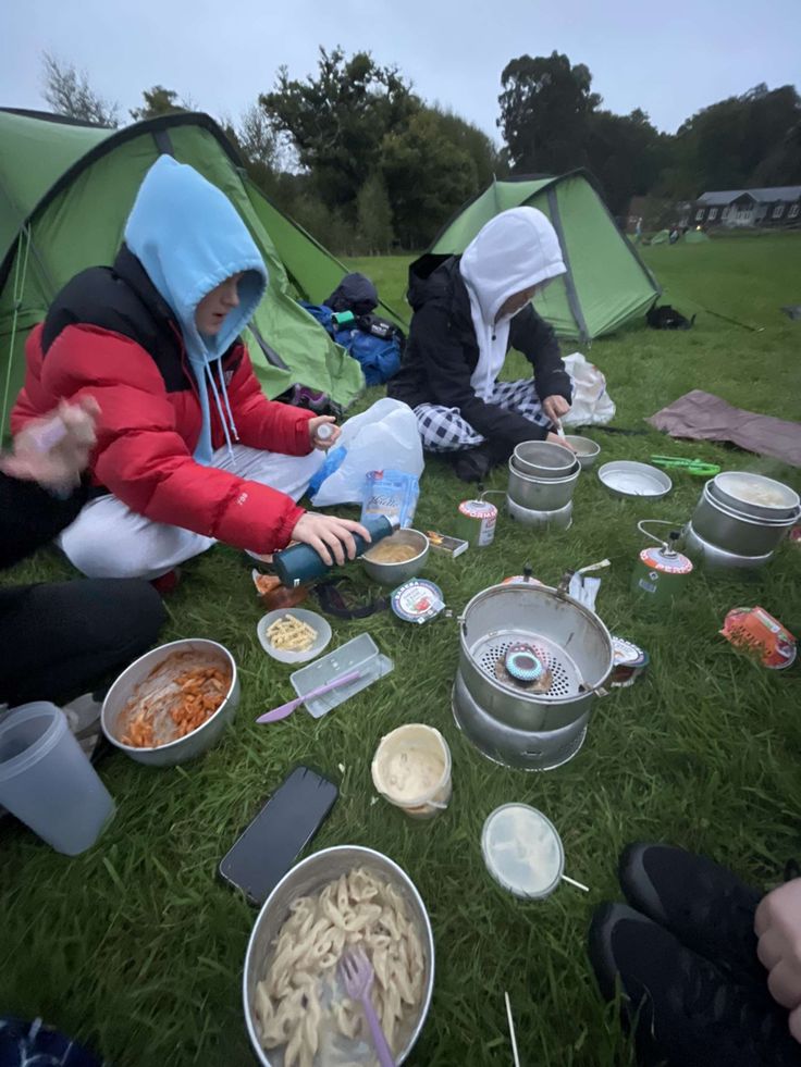 several people sitting on the grass eating food from bowls and pans in front of them