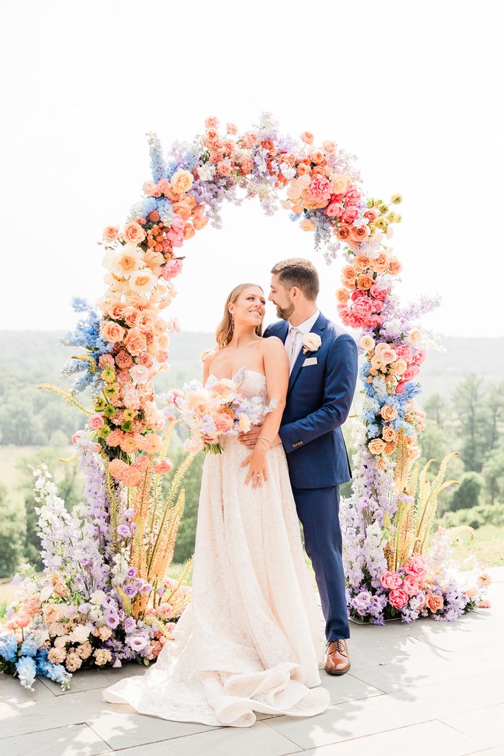 a bride and groom standing in front of an arch with colorful flowers on the side