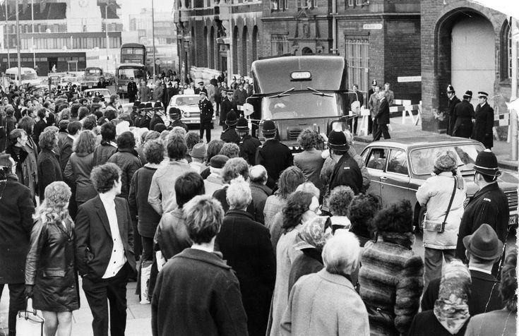 a crowd of people walking down a street next to tall brick buildings with cars and buses on them