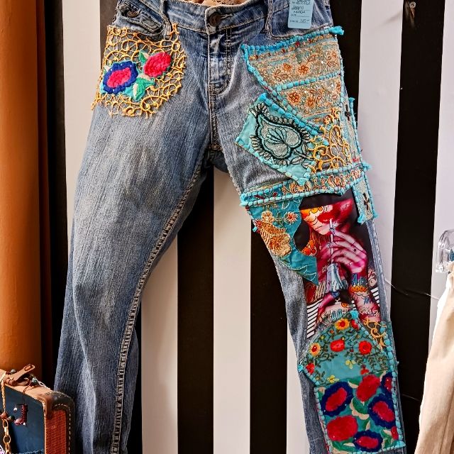 a pair of jeans with colorful patches on them hanging up against a striped wall next to a suitcase