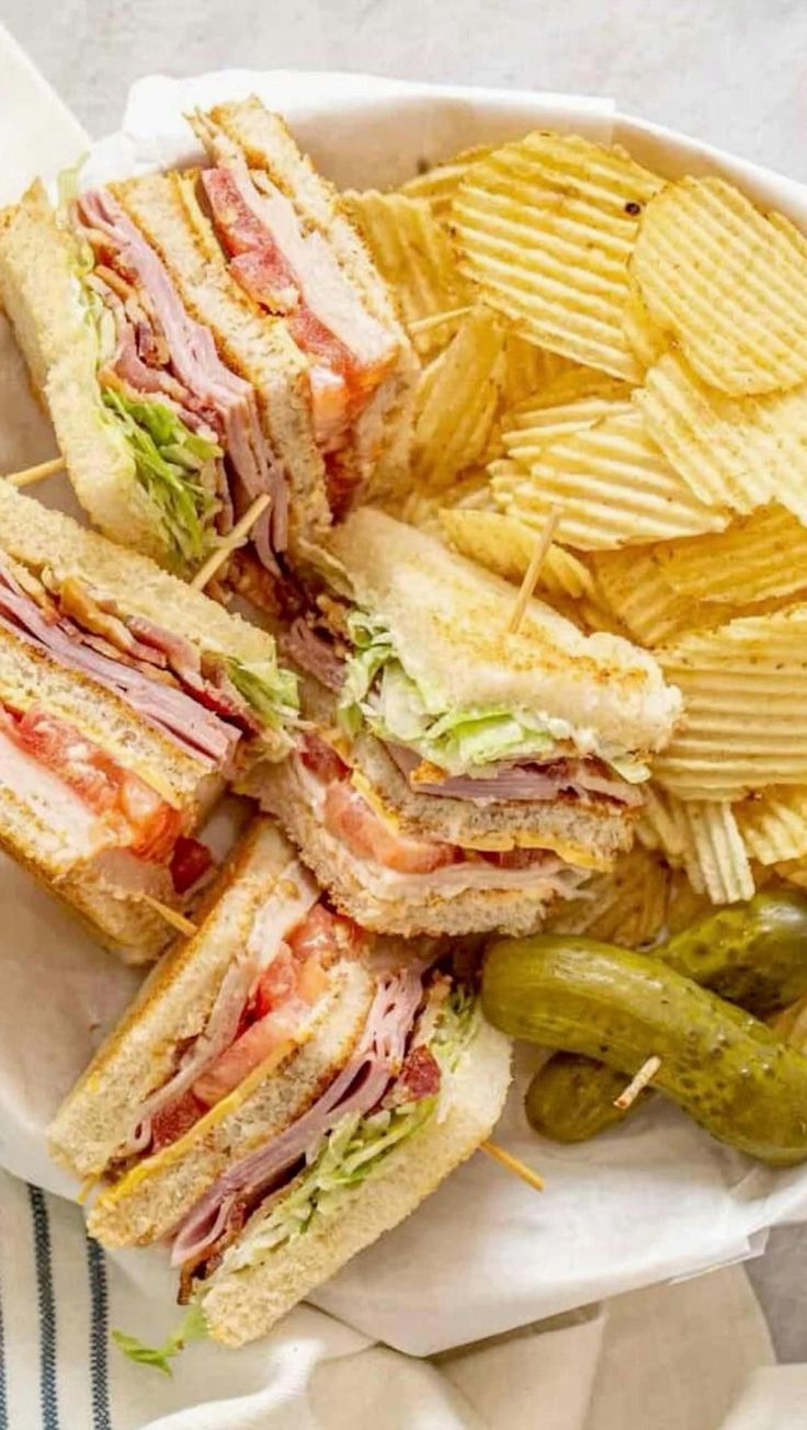 a white plate topped with a cut in half sandwich next to chips and pickles