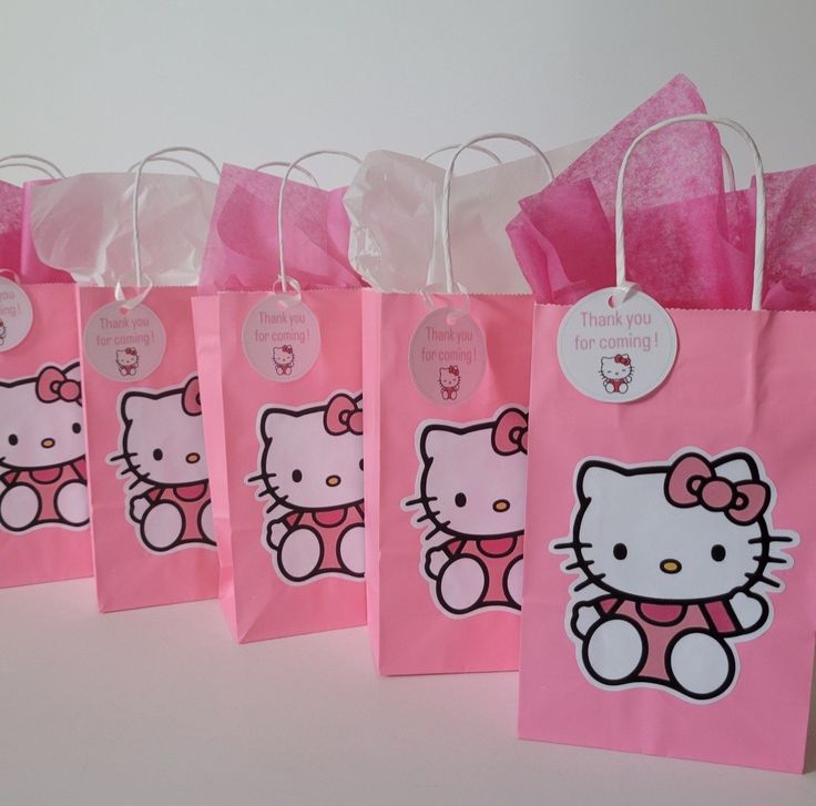 hello kitty bags are lined up on a table with pink tissue pom poms