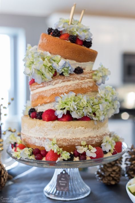 a multi layer cake sitting on top of a table next to pine cones and flowers