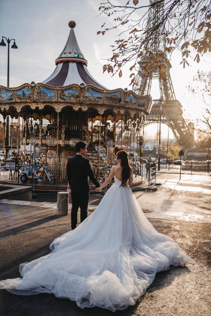 a bride and groom standing in front of a merry - go - round at sunset