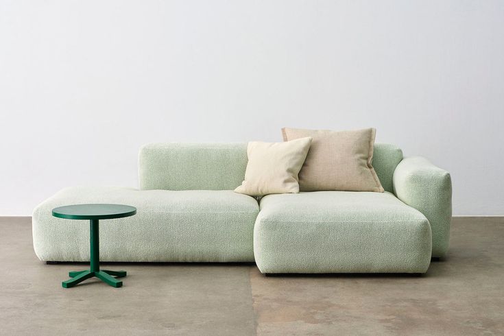 a green couch sitting on top of a cement floor next to a small round table