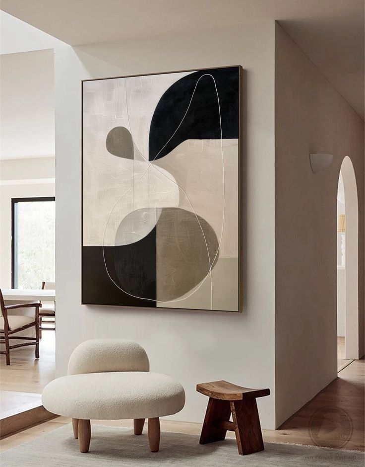 an abstract painting hangs on the wall next to a chair and ottoman