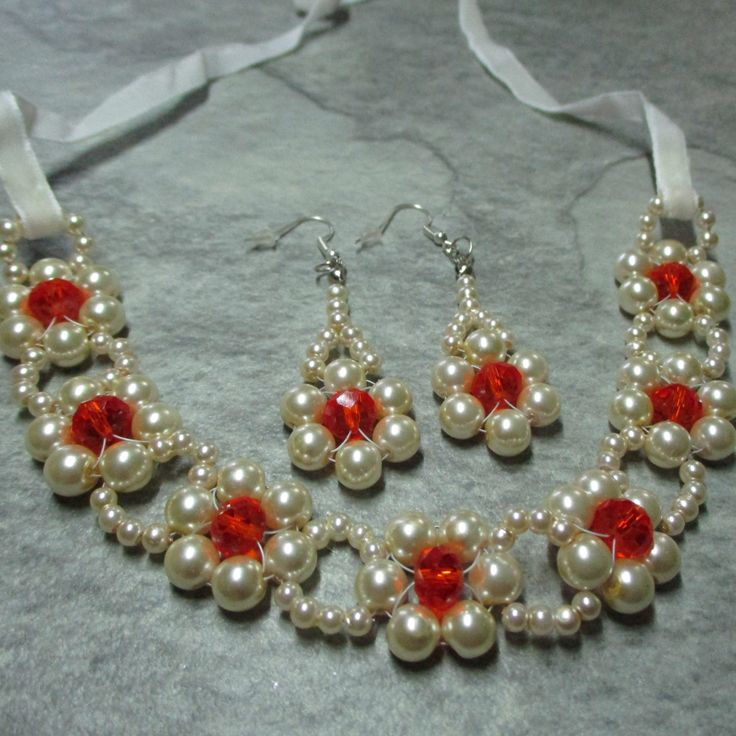 a necklace and earring set with white pearls and red glass beads on a gray background