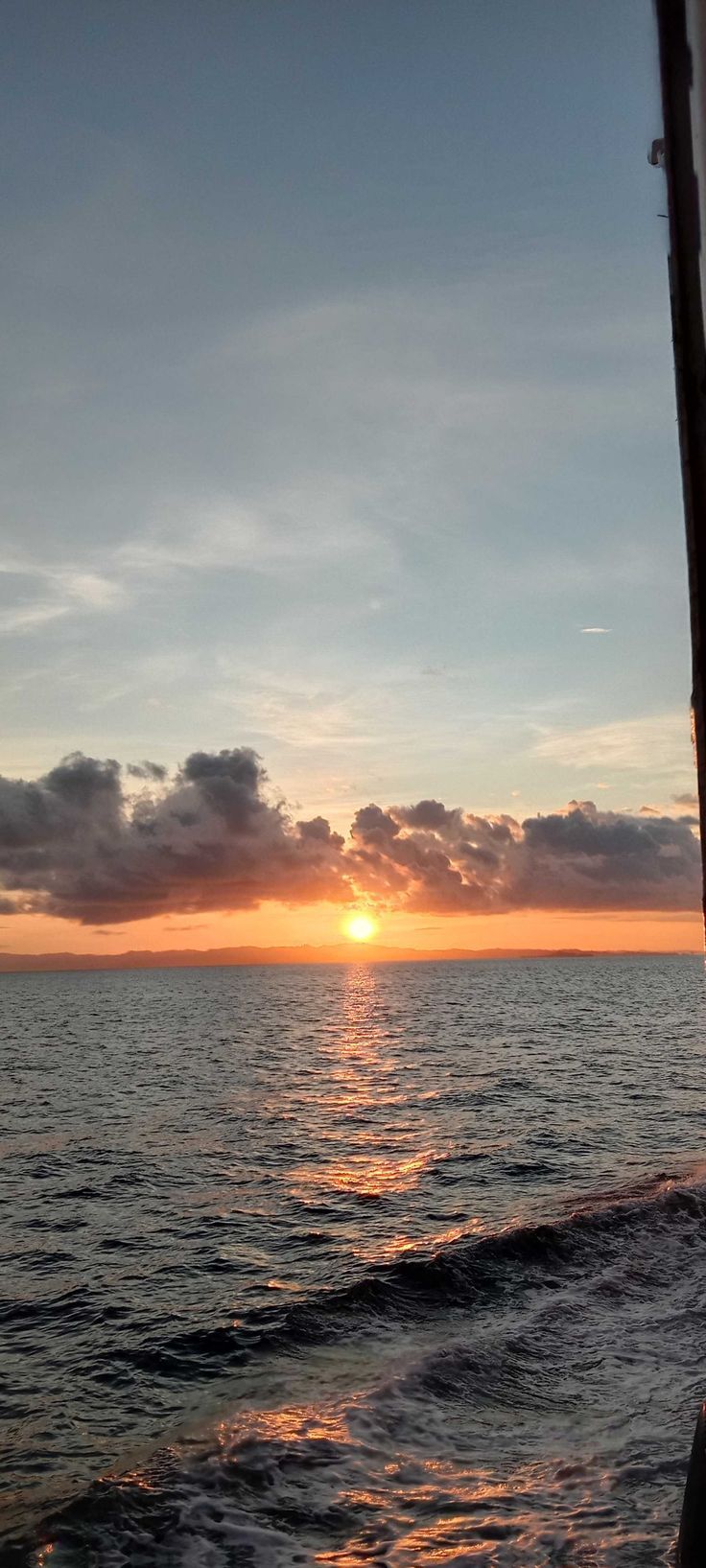 the sun is setting over the ocean as seen from a boat