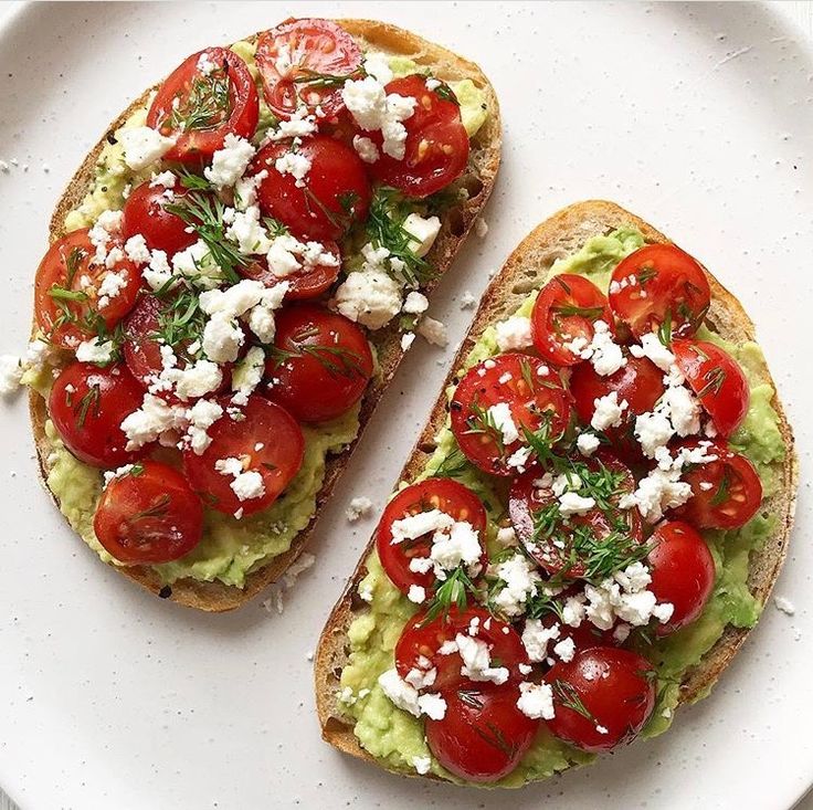 two pieces of bread with tomatoes, avocado and feta cheese on them