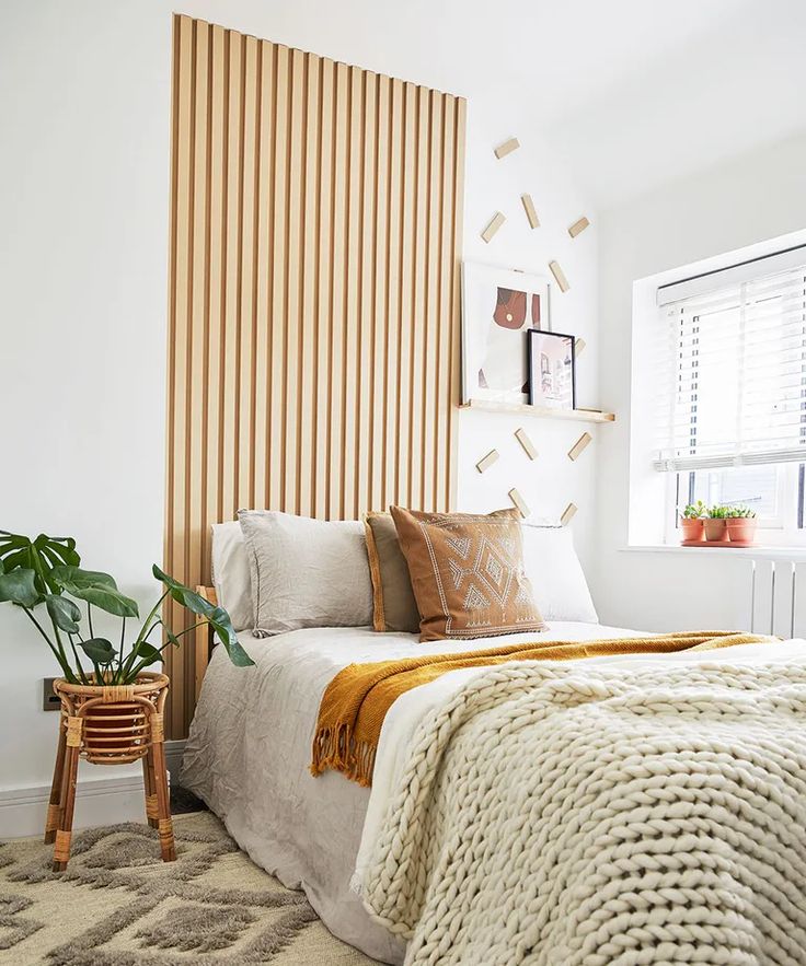 a white bed sitting next to a window in a bedroom under a wooden slatted wall