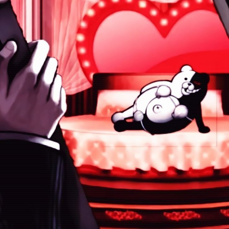 a man holding a cell phone in front of a heart - shaped bed with a teddy bear on it