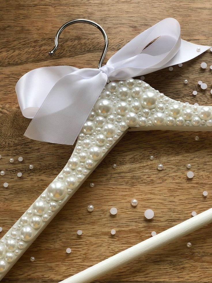 two white wedding garters on a wooden table with pearls and ribbons hanging from them