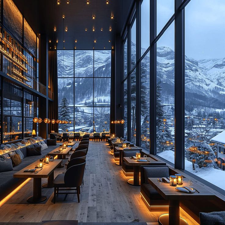 a restaurant with large windows overlooking mountains and lit up tables in front of the window