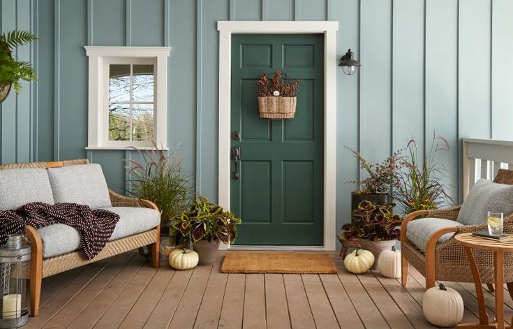 a porch with furniture and potted plants on the side walk, next to a green door