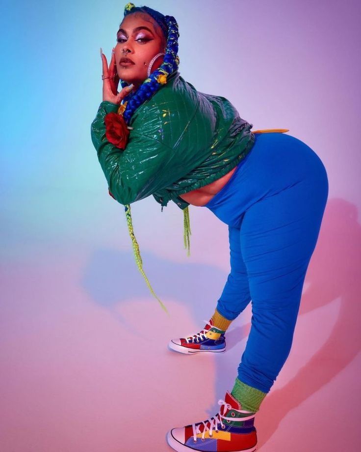 a woman in green jacket and blue pants standing on one leg with her hand up to her mouth