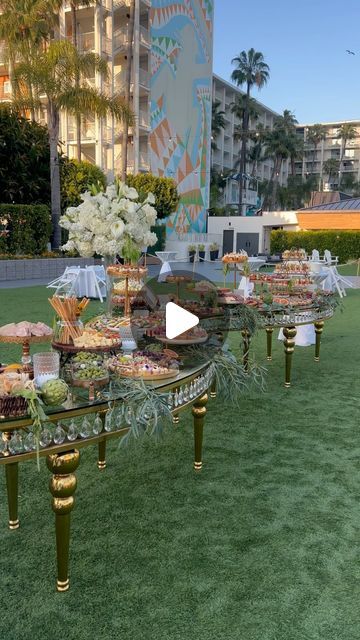 a table with many desserts on it in front of a large building and palm trees